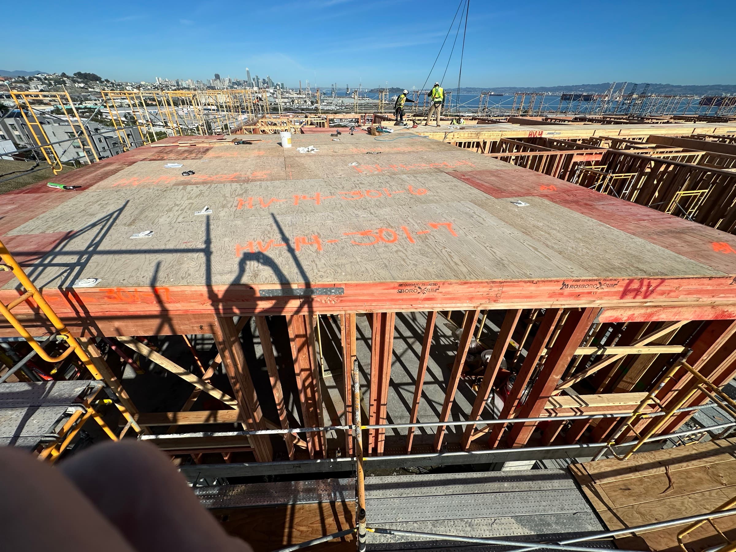 Workers standing on solid sheathed floor cassette deck with fall protection d-rings visible and San Francisco Bay in background