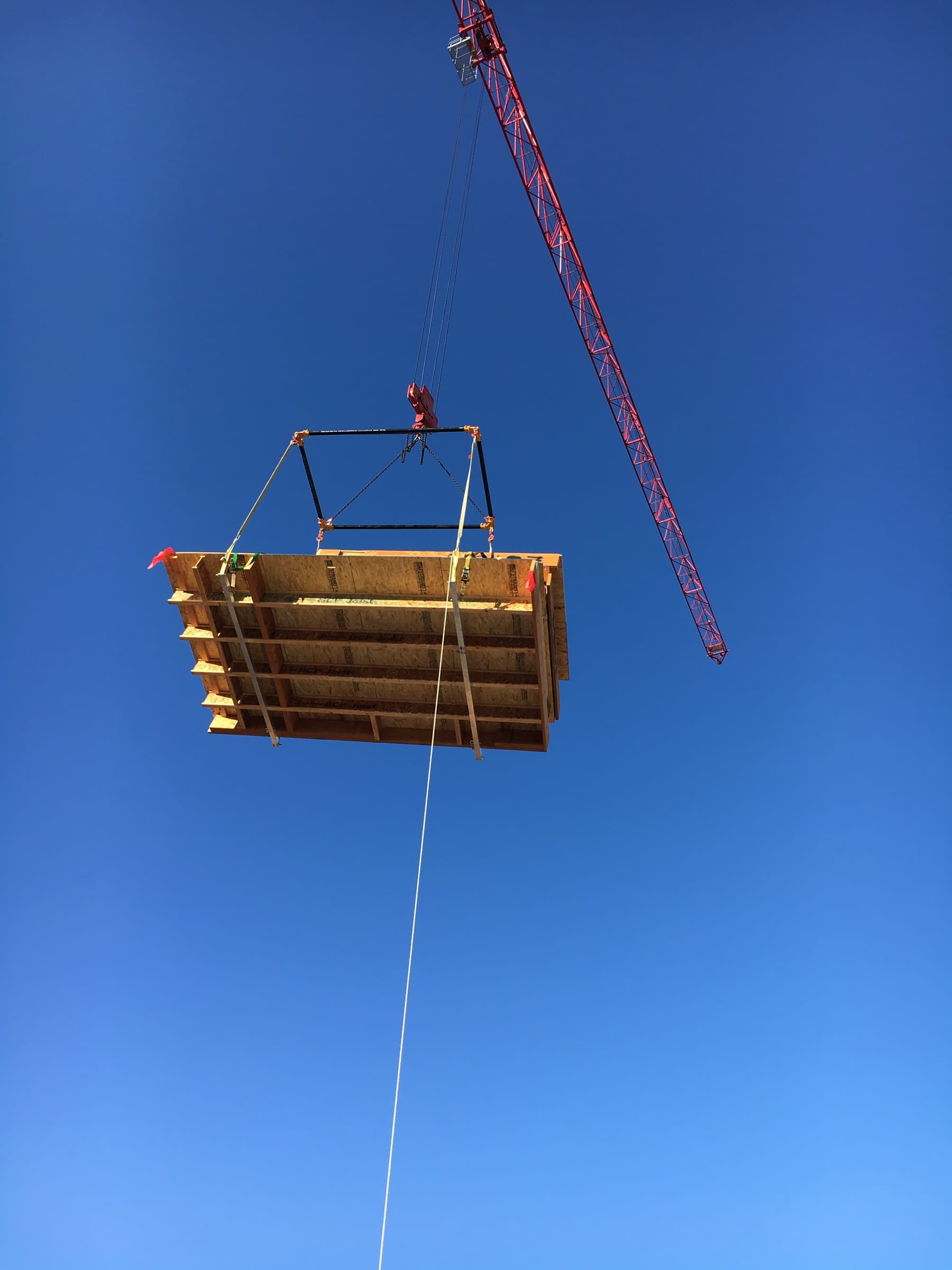 Wall panel suspended from crane against blue sky