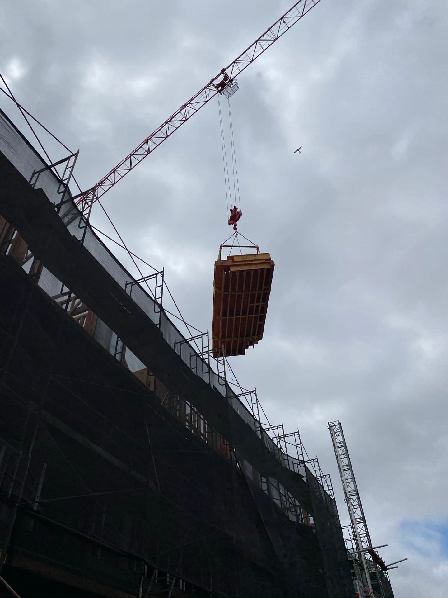 Floor cassette suspended from crane against scaffolded building viewed from below